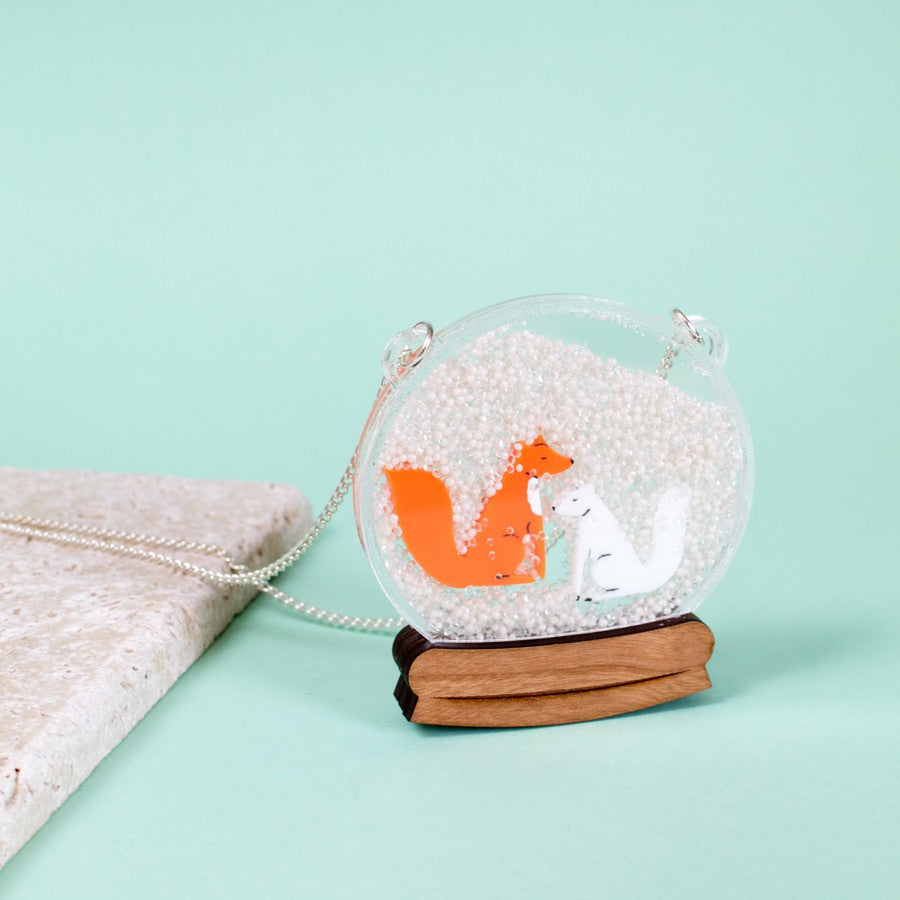 snowglobe necklace with two tiny foxes inside a snowy scene