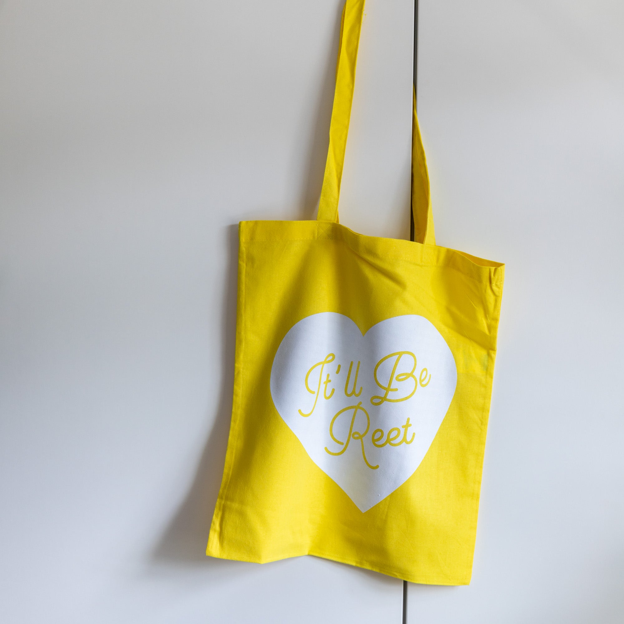Yellow tote bag with white heart and It'll be reet printed slogan